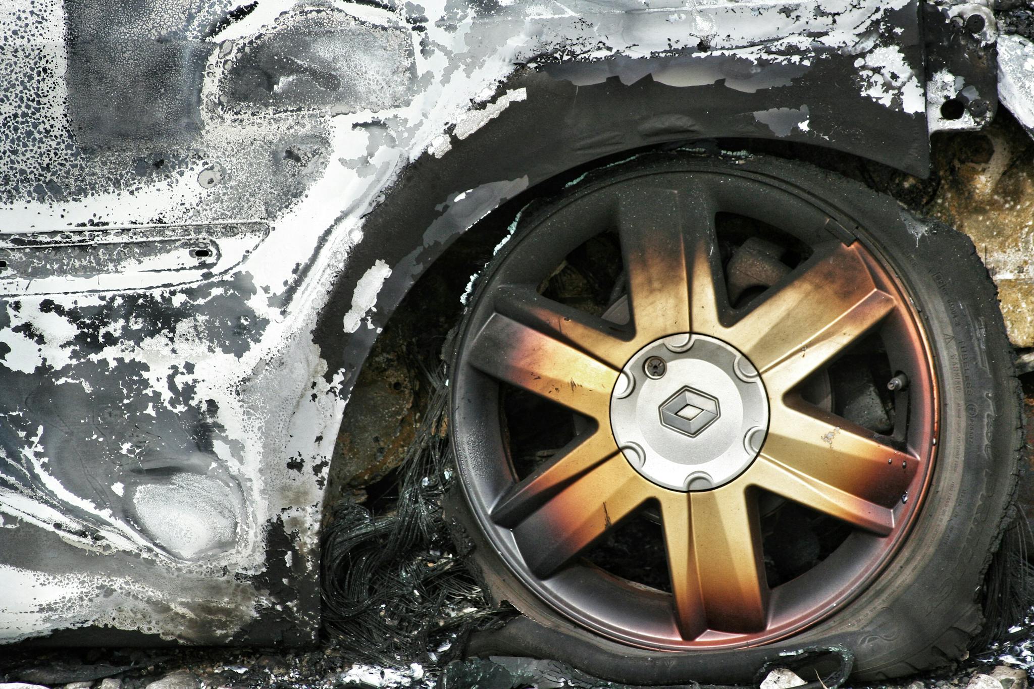 Detailed shot of a burned car wheel with rusty mag and damaged tire, showing fire aftermath.